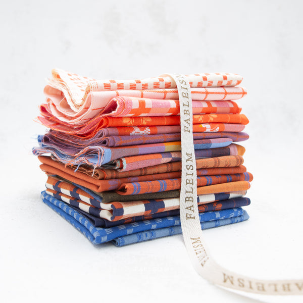 Stack of colorful fabric bundles with a visible brand ribbon on a white background
