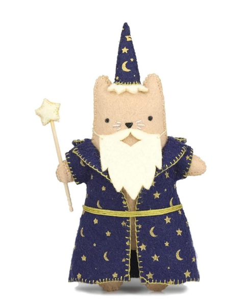 A felt wizard cat figurine wearing a navy blue robe with gold embroidered stars and moons, a cream felt beard, and a matching pointed hat, holding a star wand against a white background.