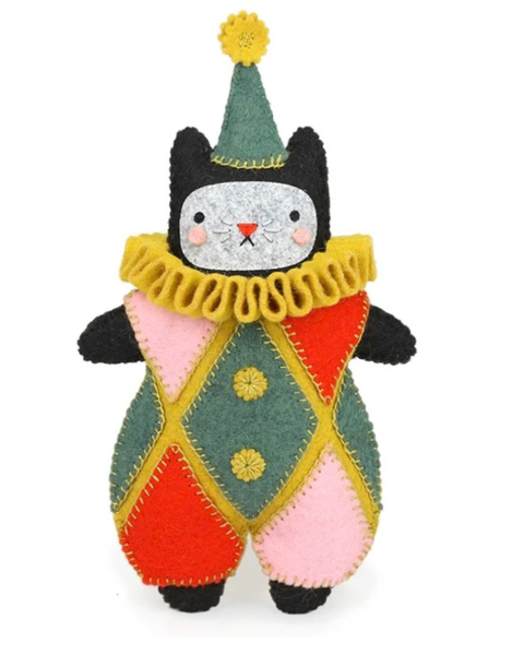 A handmade felt cat doll dressed as a jester, featuring a green hat with a yellow pom-pom, a yellow ruffled collar, and a harlequin patterned outfit in green, red, pink, and yellow on a white background.