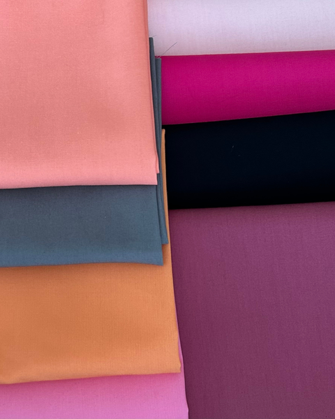 A stack of folded fabric swatches in multiple colours, including pink, grey, orange, magenta, black, and purple, arranged on a white background.