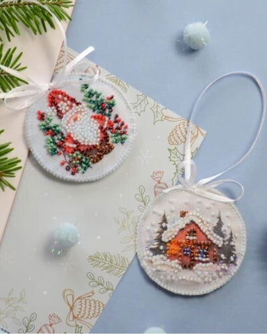 Two round embroidered Christmas ornaments on a decorative card with greenery.