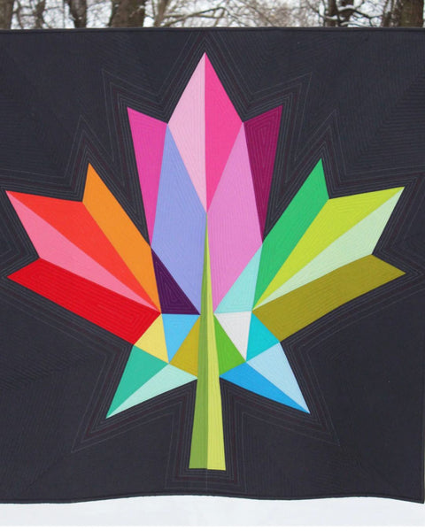 Image of multicolour maple leaf quilt on black background.