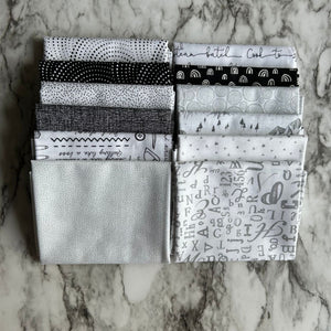A collection of black, white, and gray fat quarter fabric pieces laid out on a marble surface.