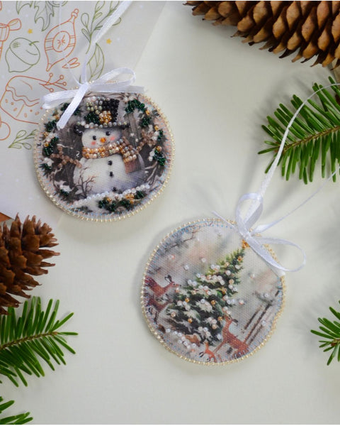 Two round Christmas ornaments with festive designs on a white surface with pine branches and cones.