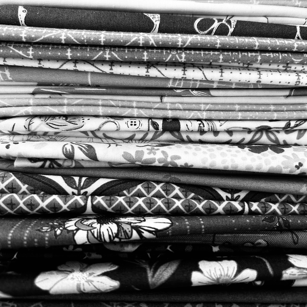 A close-up stack of folded patterned fabric pieces in black, white, and gray tones, showing various floral and geometric designs.