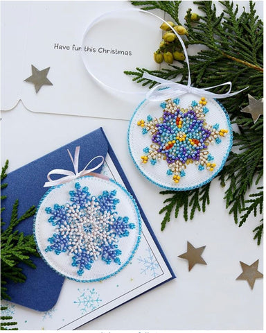 Two beaded snowflake ornaments on a table with Christmas cards, gold stars and cedar for decorations
