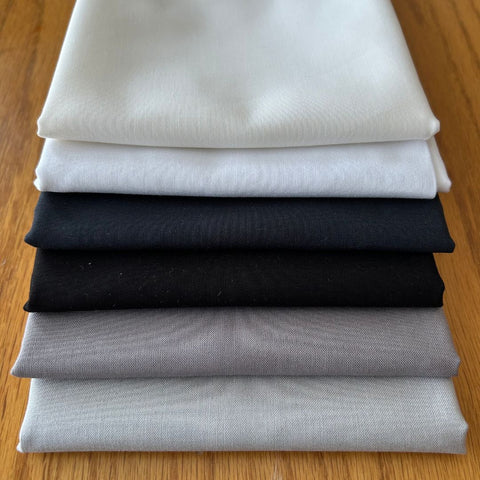 Stack of folded fabric pieces in white, black, gray, and beige on a wooden surface