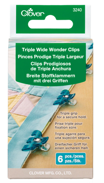 Clover brand Triple Wide Wonder Clips in a 6-pack, shown in its original retail packaging. The packaging features a green header with a hanging slot, and the front displays a quilted fabric background with blue clips demonstrating their triple-grip hold.