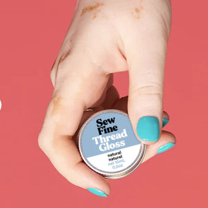 Hand holding a container of 'Sew Fine Thread Gloss' against a pink background