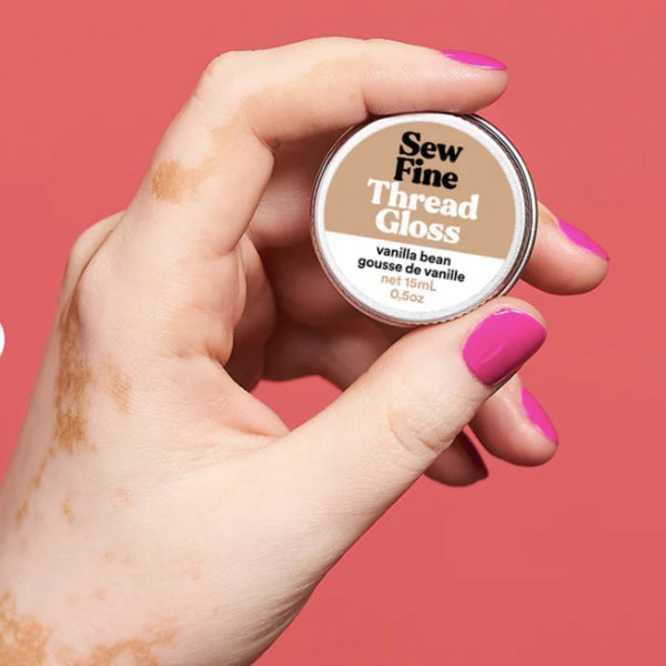 Hand holding a container of 'Sew Fine Thread Gloss' against a red background