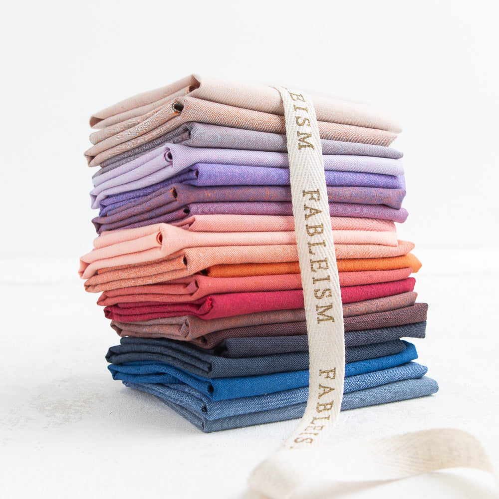 Stack of folded fabric swatches in various colors with a Fableism strap.