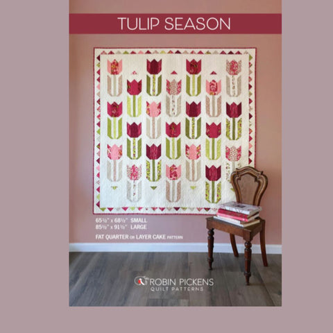 Quilt with tulip pattern on a wall, accompanied by a chair and books.